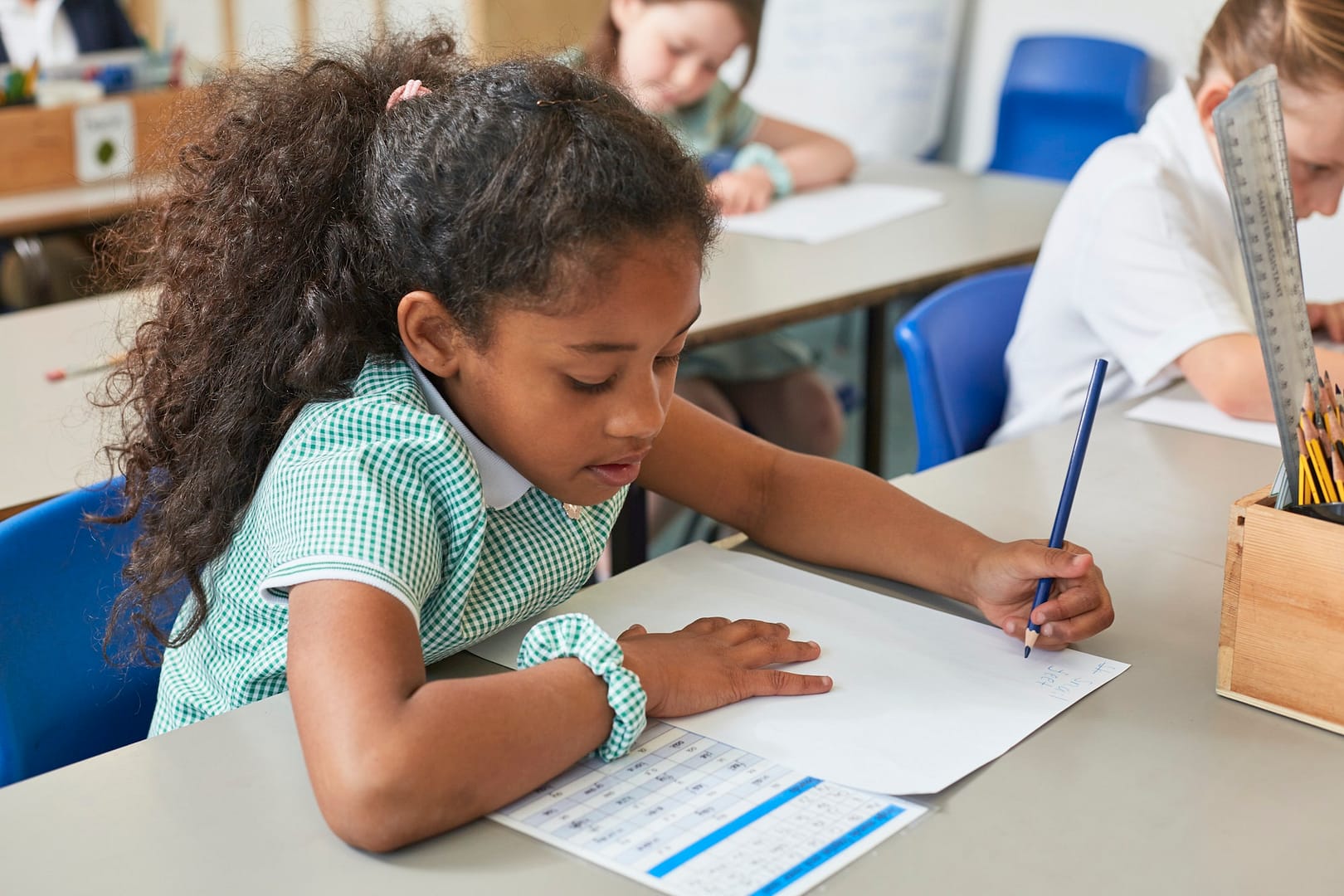 Schoolgirl writing at classroom desk in primary school lesson